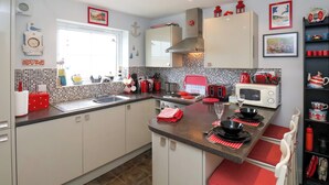 A modern kitchen with white cabinets, a tiled backsplash, and red accents. There is a window, a microwave, and a toaster on the counter.