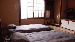 Una habitación con dos camas, una ventana con persianas, un ventilador y una estantería con un objeto decorativo.