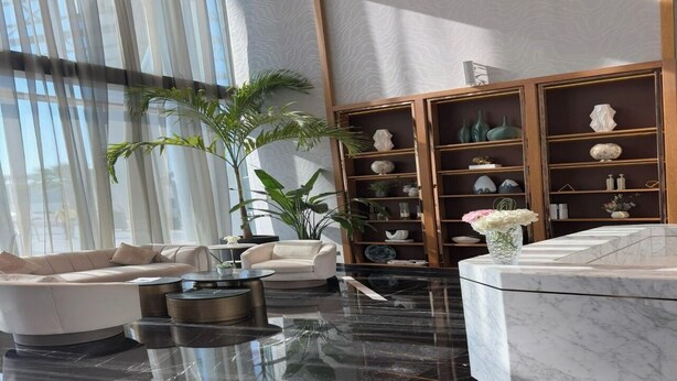 A modern living room with a marble floor, white sofas, a coffee table, and a bookshelf with decorative items. - Aykon City Stylish 2 BHK Beach Bay View (Dubai)