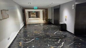 A hotel corridor with a marble floor, a trash bin, and a potted plant. - Aykon City Stylish 2 BHK Beach Bay View (Dubai)