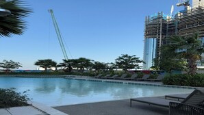 A swimming pool with lounge chairs and a construction crane in the background. - Aykon City Stylish 2 BHK Beach Bay View (Dubai)