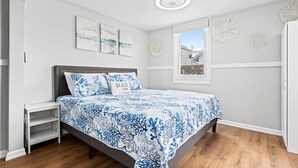 Een slaapkamer met een bed, nachtkastje, raam en wanddecoraties.