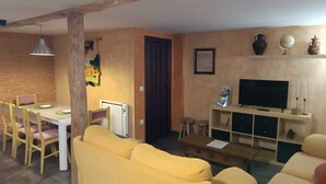 Ein Wohnzimmer mit gelben Sofas, einem Essbereich mit Tisch und Stühlen, einem Fernseher und einem Kamin.