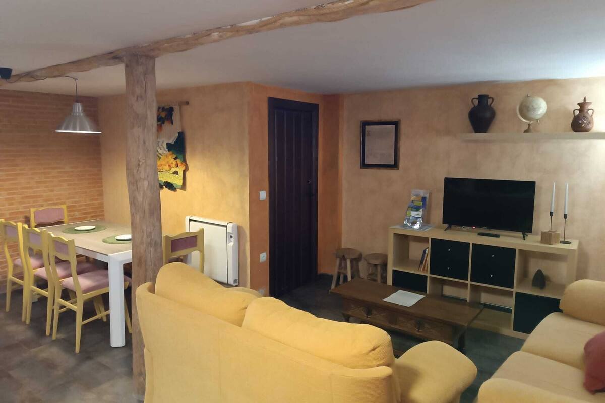 A living room with yellow sofas, a dining area with a table and chairs, a TV, and a fireplace.