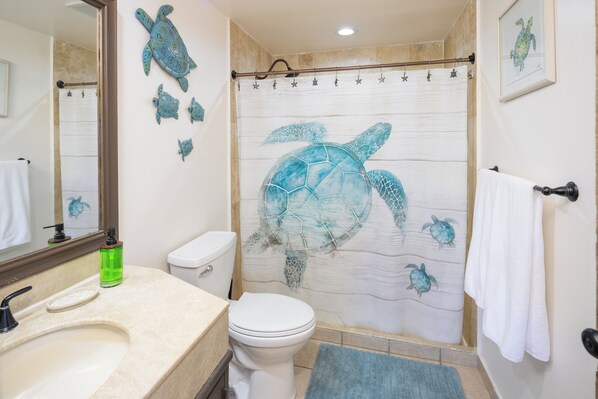 A bathroom with a large turtle mural on the shower curtain, a white toilet, a sink with a green soap dispenser, and a towel rack. - BeachBumCondos (Puerto Peñasco)