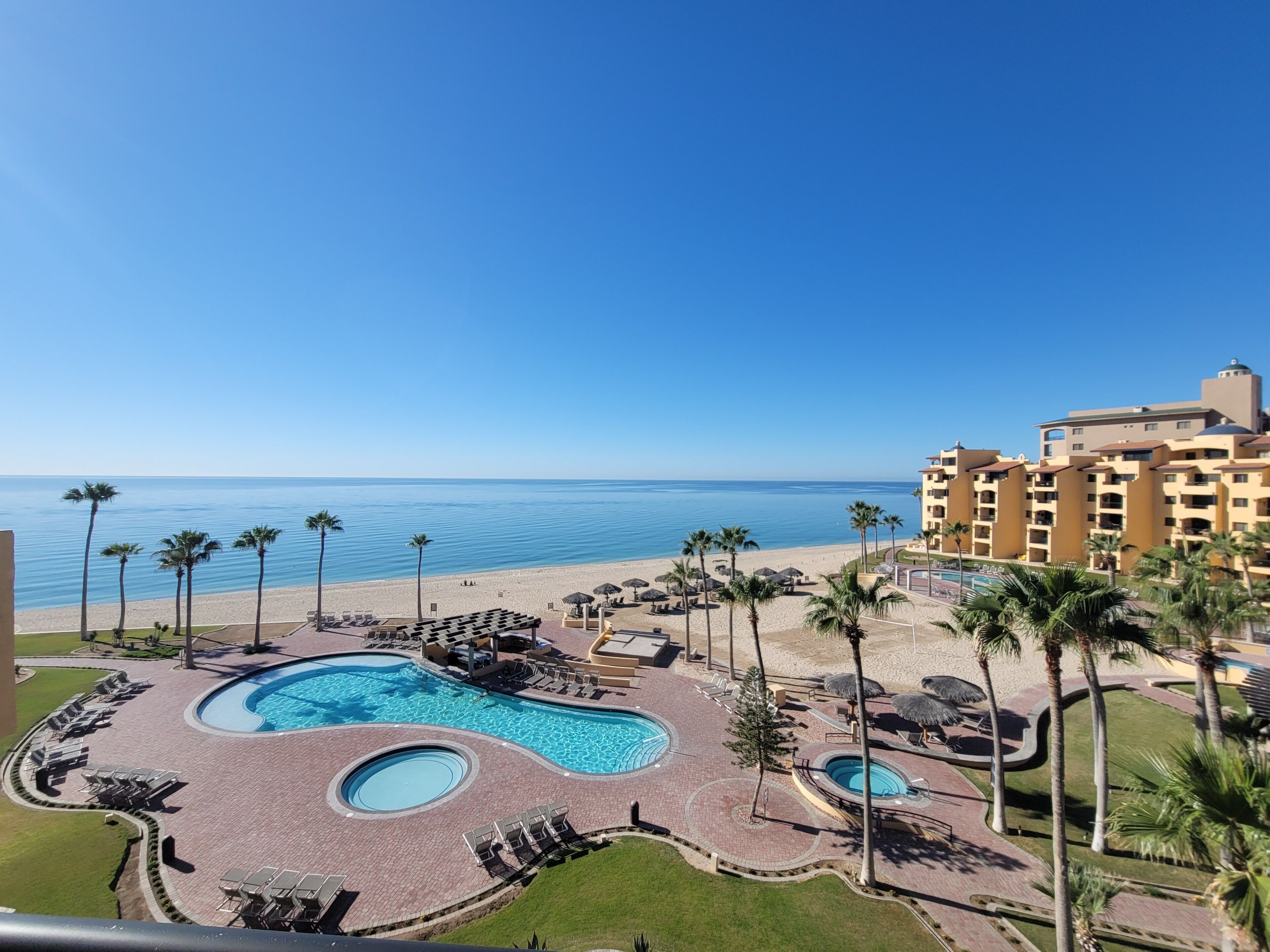 A resort with a pool area, palm trees, and a beach view.