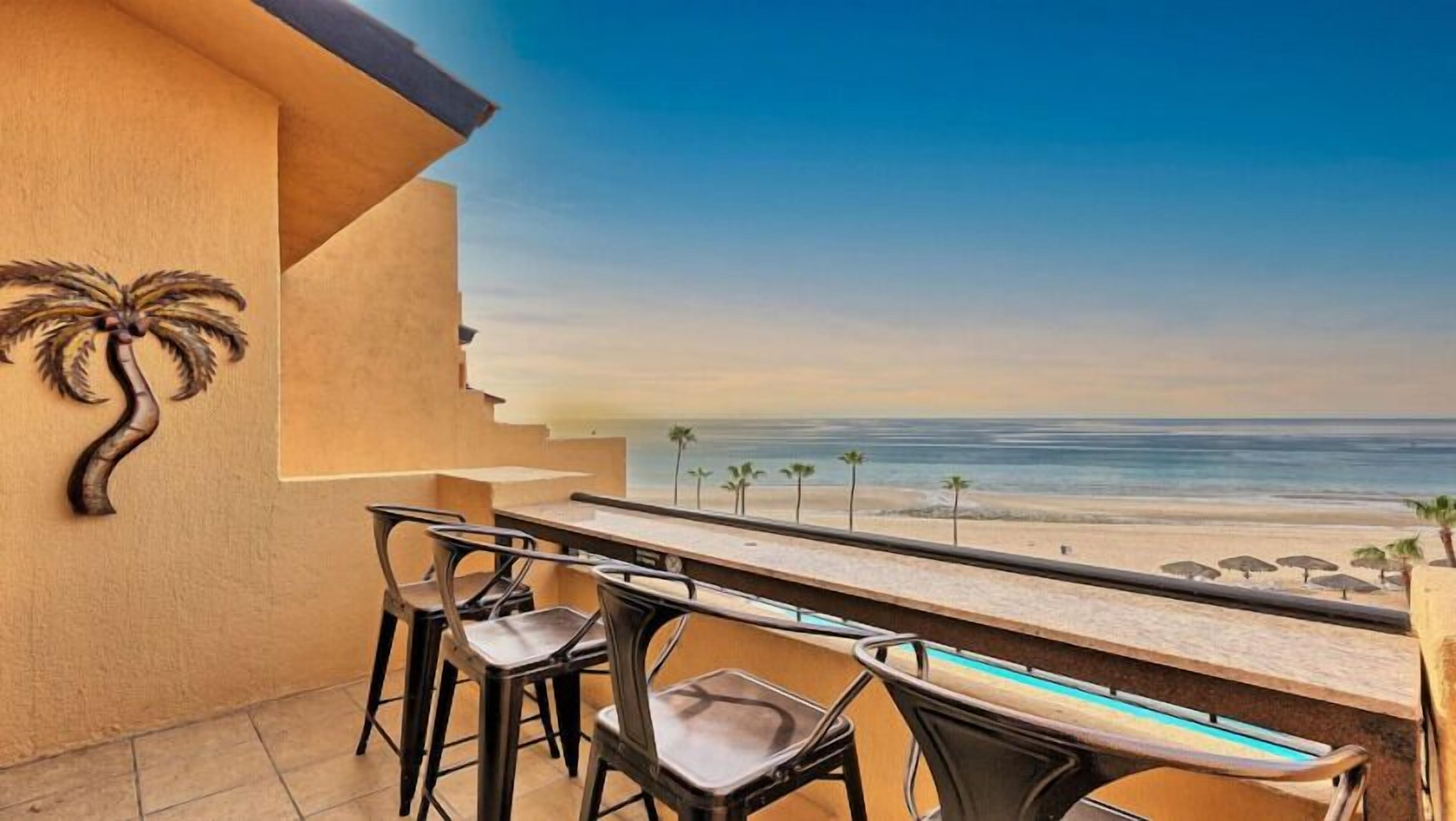 A balcony with a view of the beach, featuring a pool table and bar stools.
