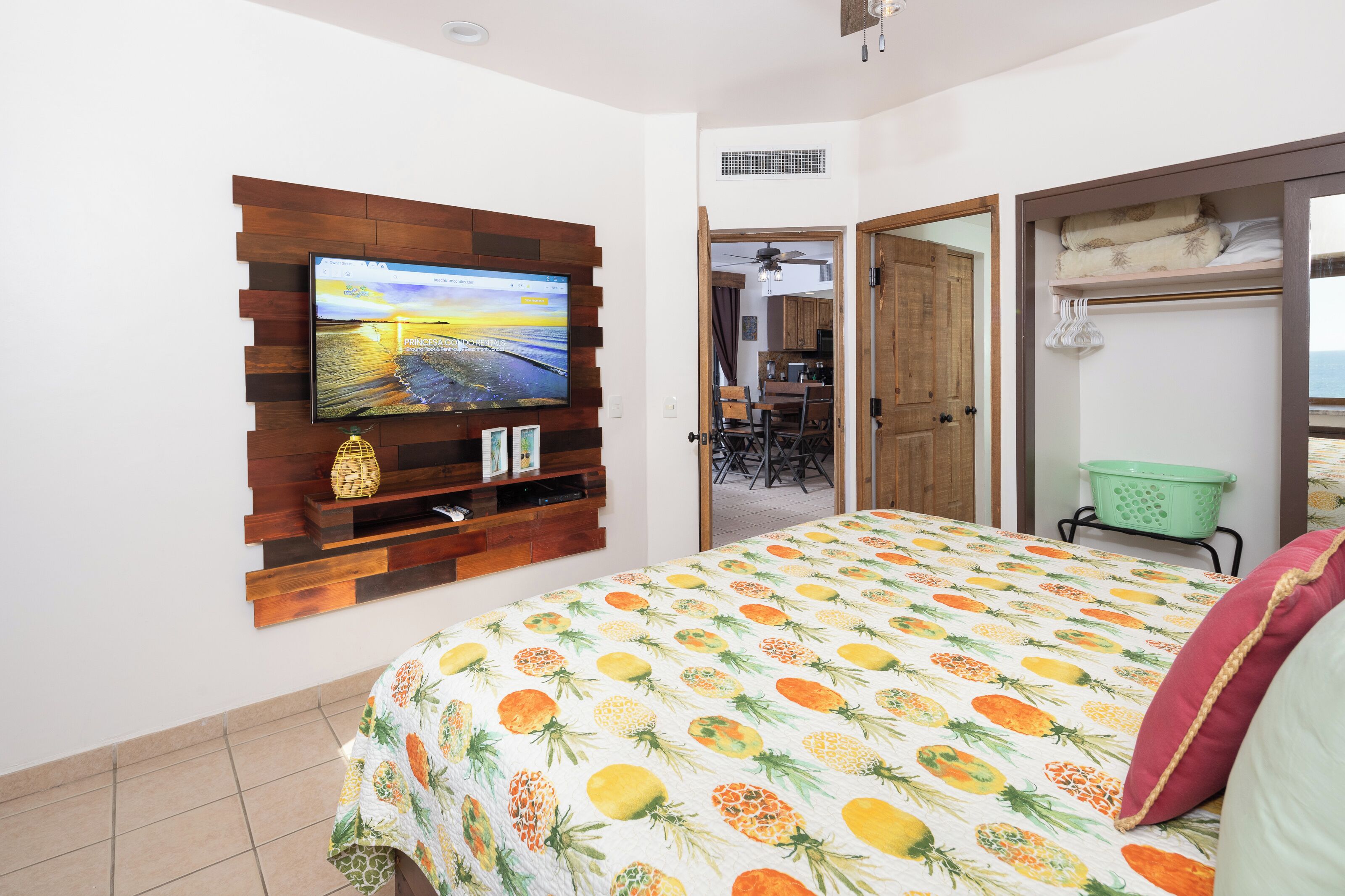 Un dormitorio con cama, televisor montado en un panel de madera, una cesta verde y un armario.