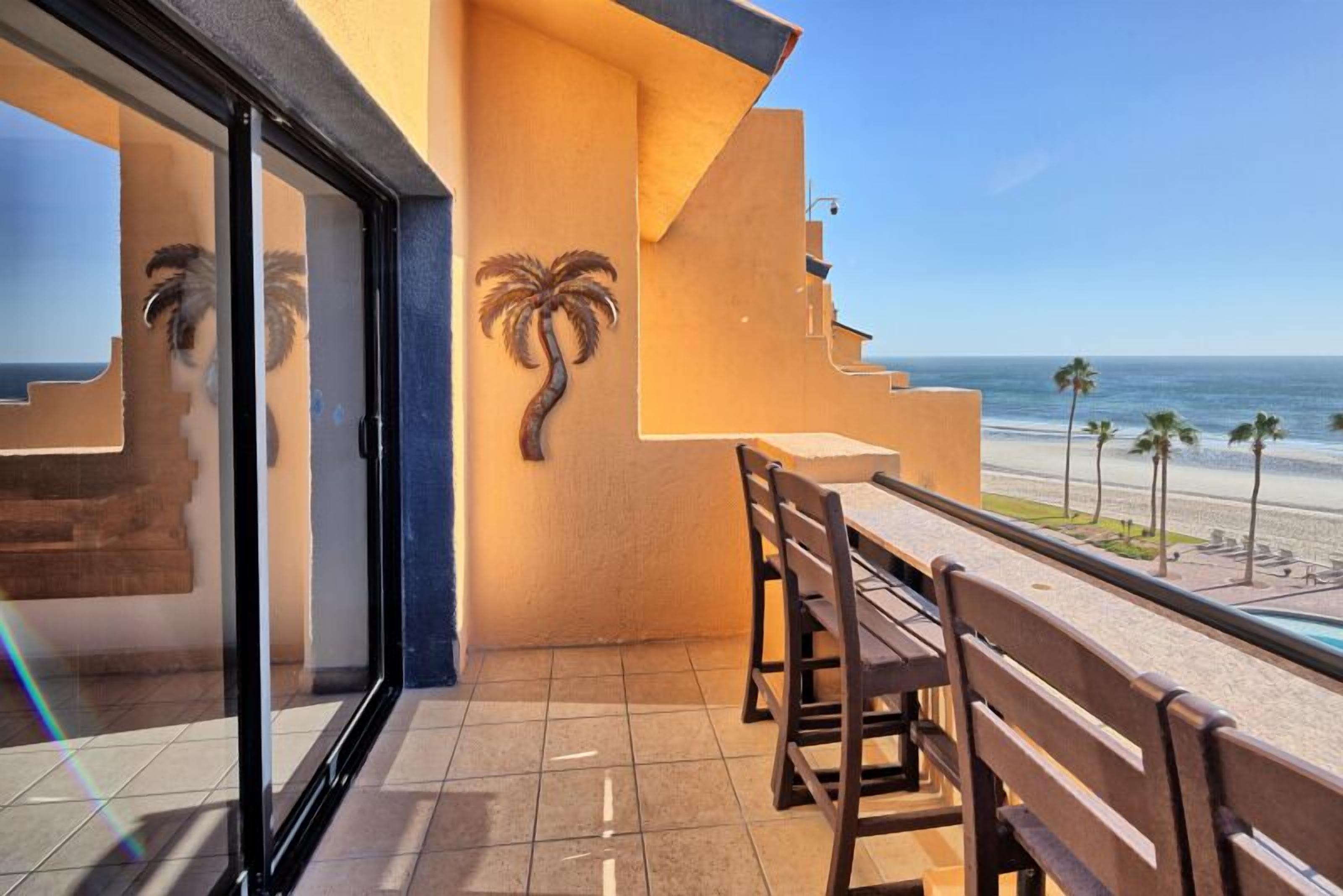 Un balcón con vista a la playa, decoración con palmera y puerta de cristal.