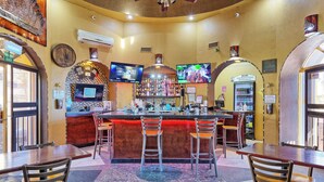 A bar area with a counter, stools, and a television screen. - BeachBumCondos (Puerto Peñasco)