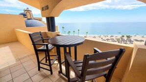 A balcony with a round table and two chairs, overlooking a beach with umbrellas and palm trees. - BeachBumCondos (Puerto Peñasco)