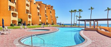 A swimming pool with a curved design, surrounded by a brick walkway and palm trees.