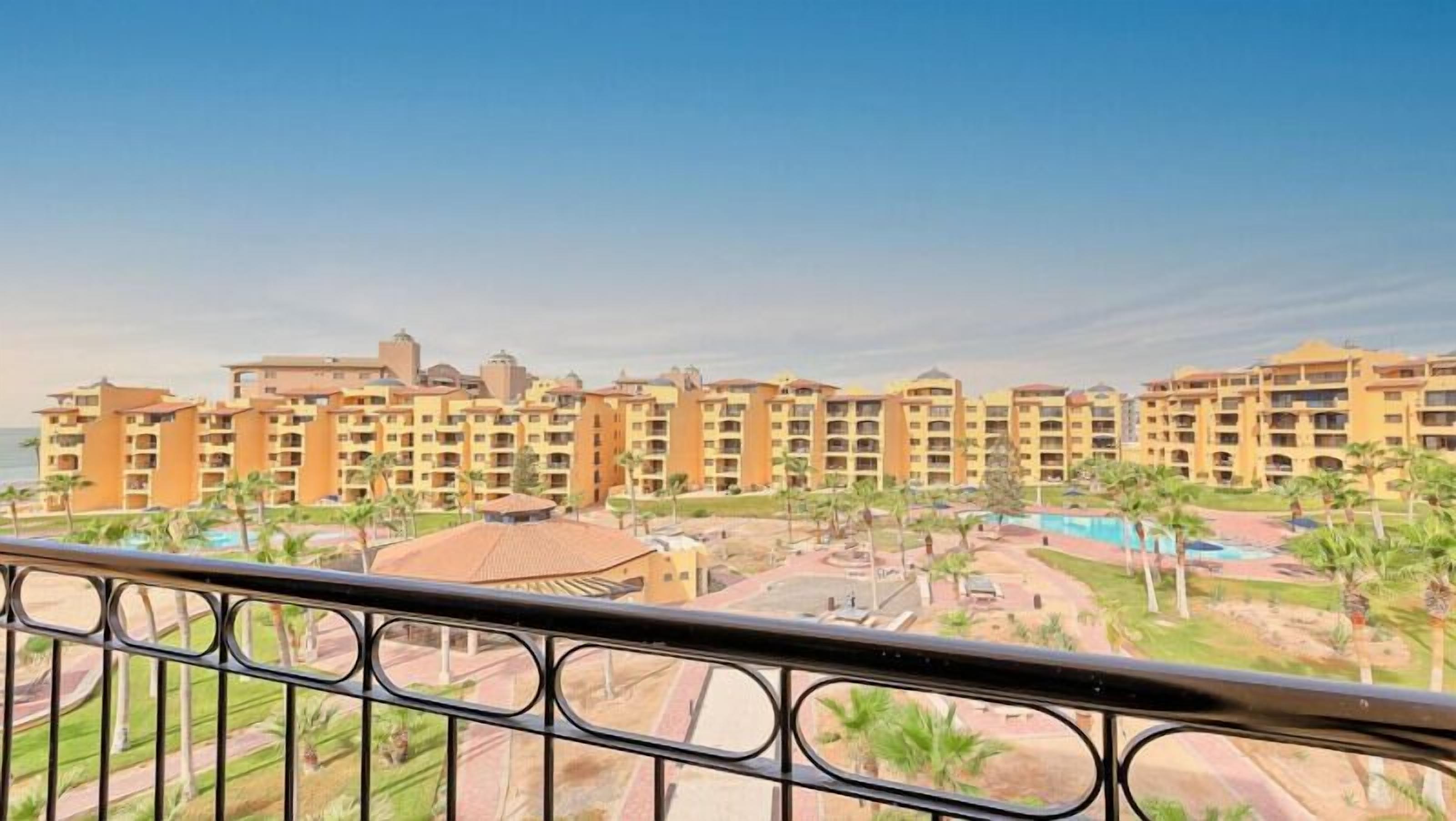 A hotel with multiple buildings, a swimming pool, and a landscaped area with palm trees.