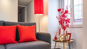 A modern living room with a grey sofa, red cushions, a red floor lamp, and a small table with decorative items.
