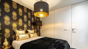 A bedroom with a black and gold pineapple wallpaper, a black and gold bed, and a black pendant light.