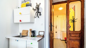 Une cuisine moderne avec des meubles blancs, un évier et une machine à café. On y trouve une planche à découper en bois et un petit tableau encadré posé sur le comptoir.