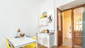 Une cuisine de taille modeste, dotée d’un plan de travail blanc, de chaises jaunes et d’une porte en bois donnant sur une autre pièce.