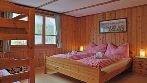 Une pièce en bois avec un lit superposé, un lit simple avec une couette à carreaux, un tableau au mur et une fenêtre avec des rideaux.