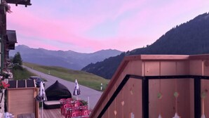 Une terrasse en bois avec des chaises rouges et une tente noire, d’où l’on a vue sur une route et des montagnes.
