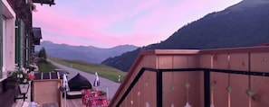 Une terrasse en bois avec des chaises rouges et une tente noire, d’où l’on a vue sur une route et des montagnes.