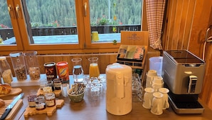 Une table en bois dressée pour le petit-déjeuner, avec des machines à café, du thé et divers aliments.