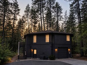 A two-story cabin with a dark exterior, a front door, and a garage. - 1-Acre Forest Sanctuary | Hot Tub | Seasonal Creek (Idyllwild-Pine Cove)