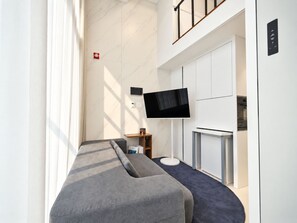 A modern hotel room with a large flat-screen TV mounted on the wall, a sofa, and a small table with a lamp. - UH FLAT SIGNATURE GANGNAM (Seoul)
