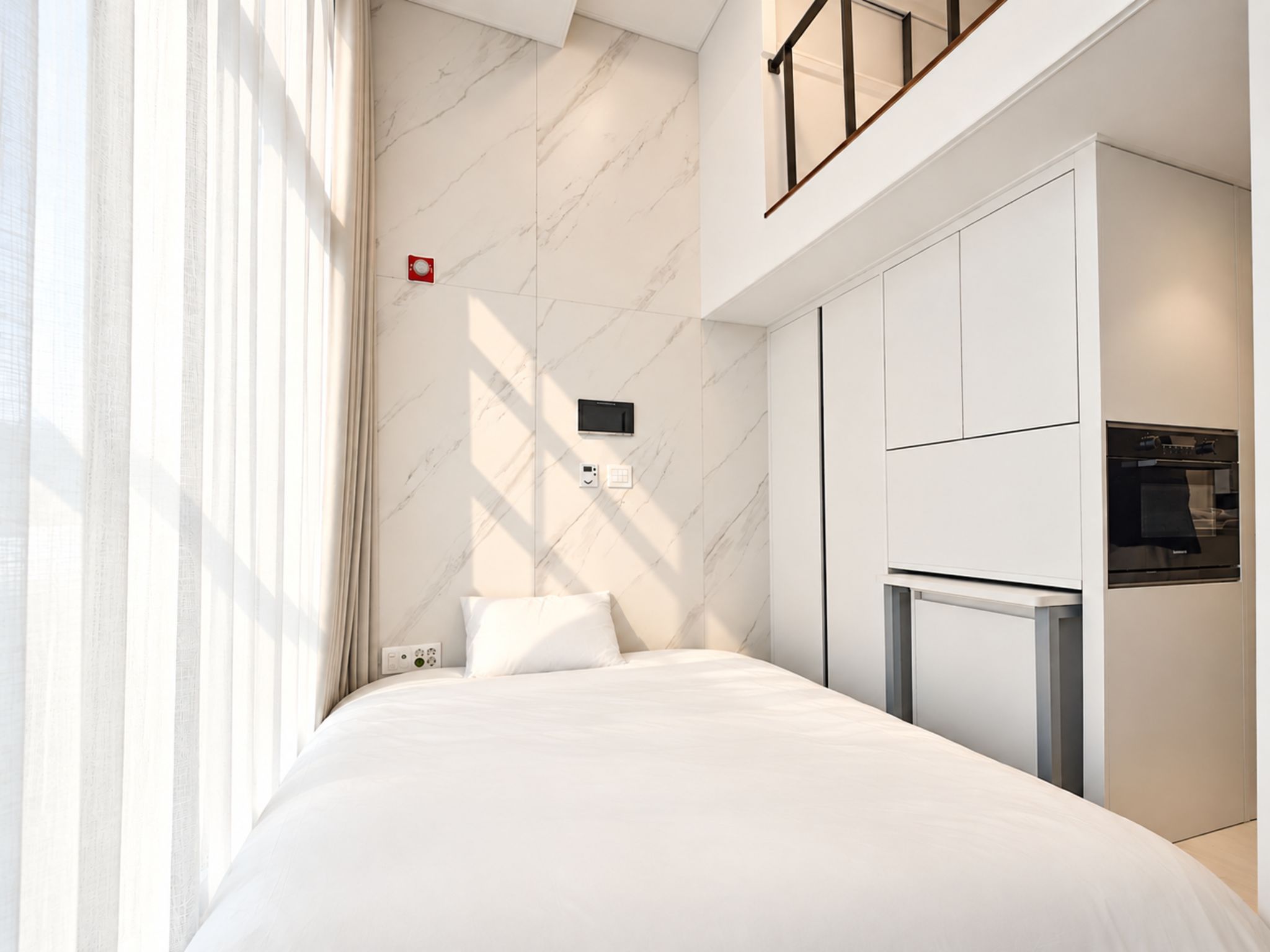 A modern hotel room with a bed, a built-in TV, and a microwave.