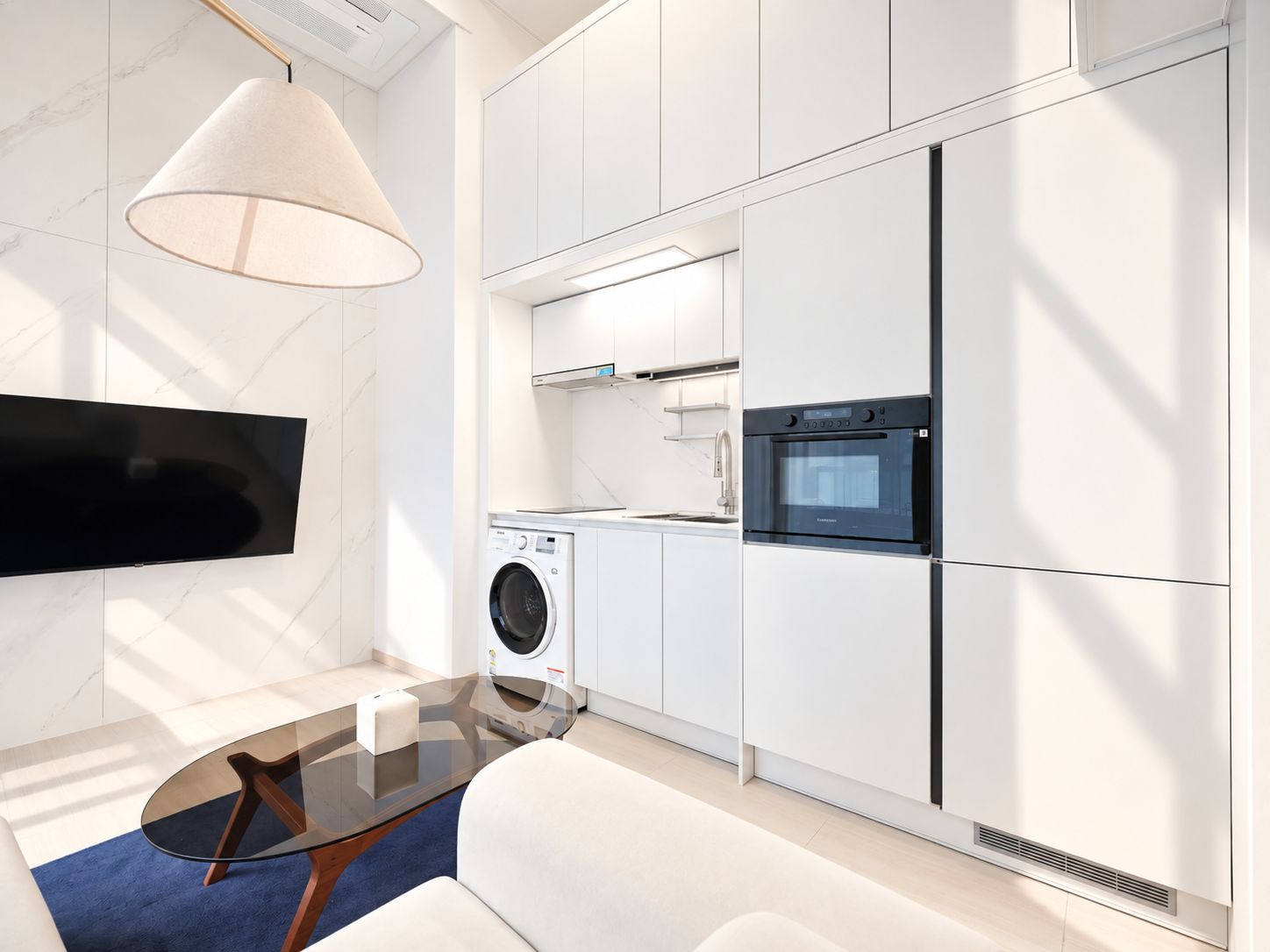 A modern kitchen with a built-in oven, a washing machine, and a flat-screen TV mounted on the wall.