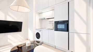 A modern kitchen with a built-in oven, a washing machine, and a flat-screen TV mounted on the wall.