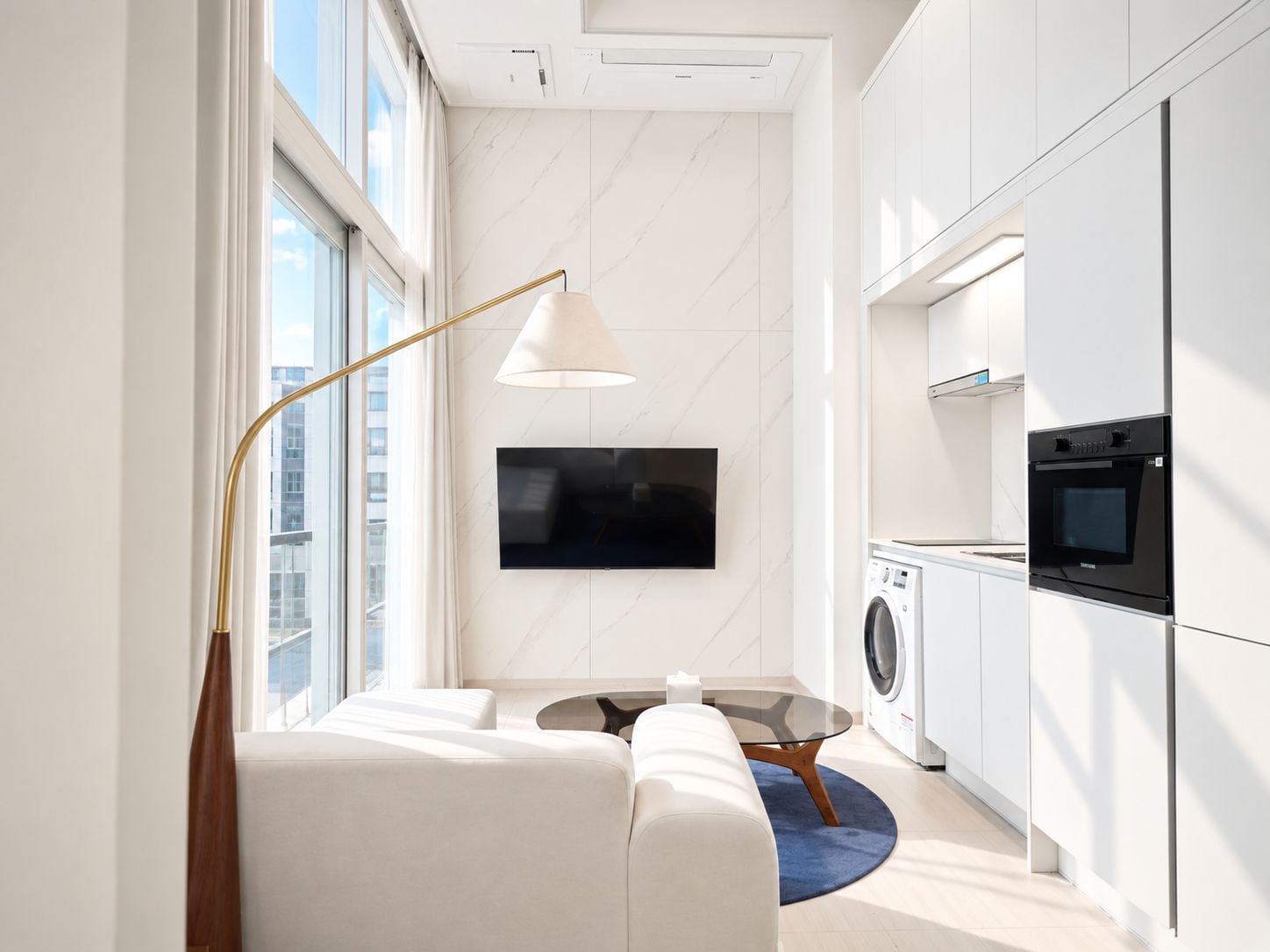 A modern kitchen with built-in appliances, a flat-screen TV, and a sofa in a bright living area with a large window.