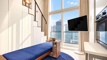 Una habitación moderna con una cama, un televisor, una mesita y una ventana con vistas a la ciudad.