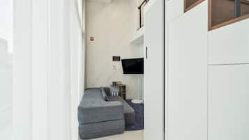 A modern, compact room with a grey sectional sofa, a flat-screen TV mounted on the wall, and a small side table with a lamp.