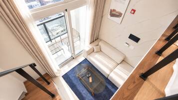 A modern living room with a sofa, a coffee table, and a view through a large window.