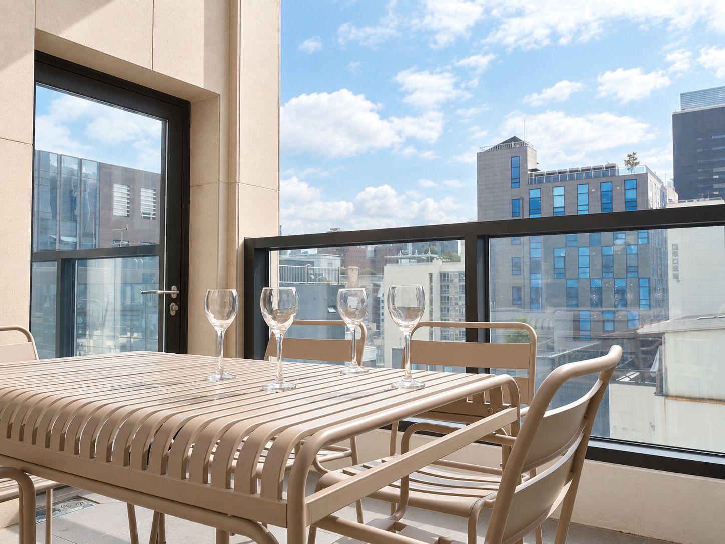 A balcony with a table and chairs, a glass door, and a city view.