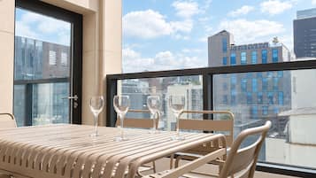 A balcony with a table and chairs, a glass door, and a city view.