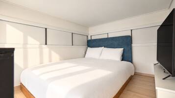 Quarto moderno com cama grande, televisão de tela plana e piso de madeira.