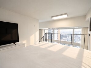 A hotel room with a large bed, a TV mounted on the wall, and a city view through the window. - UH FLAT SIGNATURE GANGNAM (Seoul)