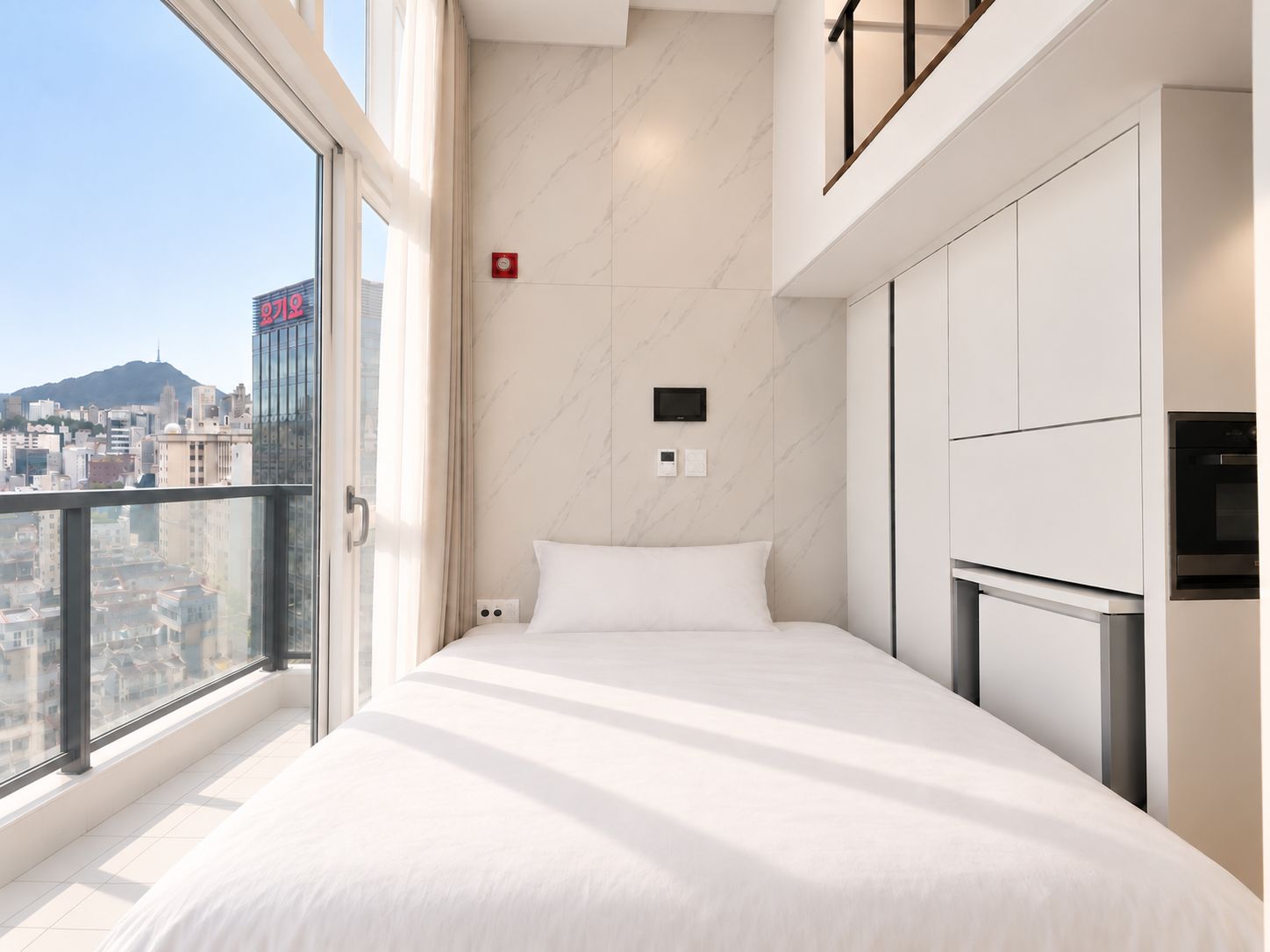 A modern hotel room with a bed, a TV, and a view of the cityscape.