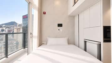 A modern hotel room with a bed, a TV, and a view of the cityscape.
