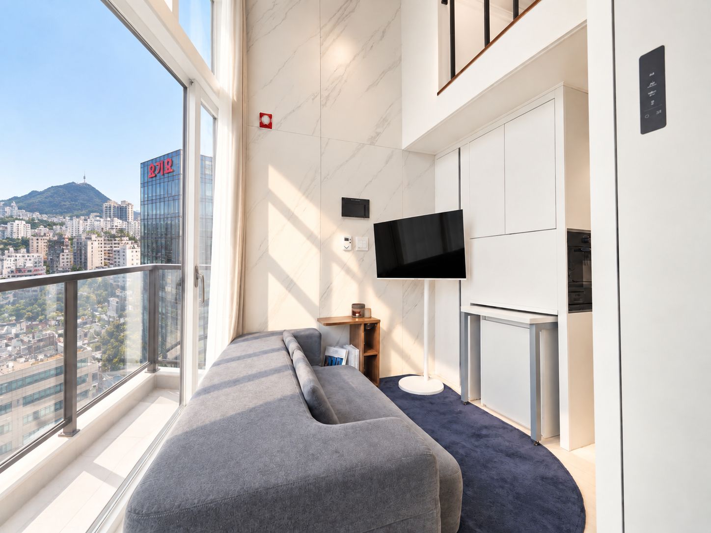 Una habitación de hotel moderna con un gran ventanal, televisor de pantalla plana, sofá y minibar.