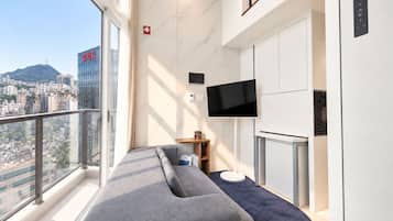 Una habitación de hotel moderna con un gran ventanal, televisor de pantalla plana, sofá y minibar.