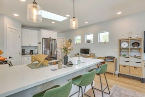 Una cocina moderna con armarios blancos, una isla grande con taburetes de bar, un refrigerador e iluminación colgante.