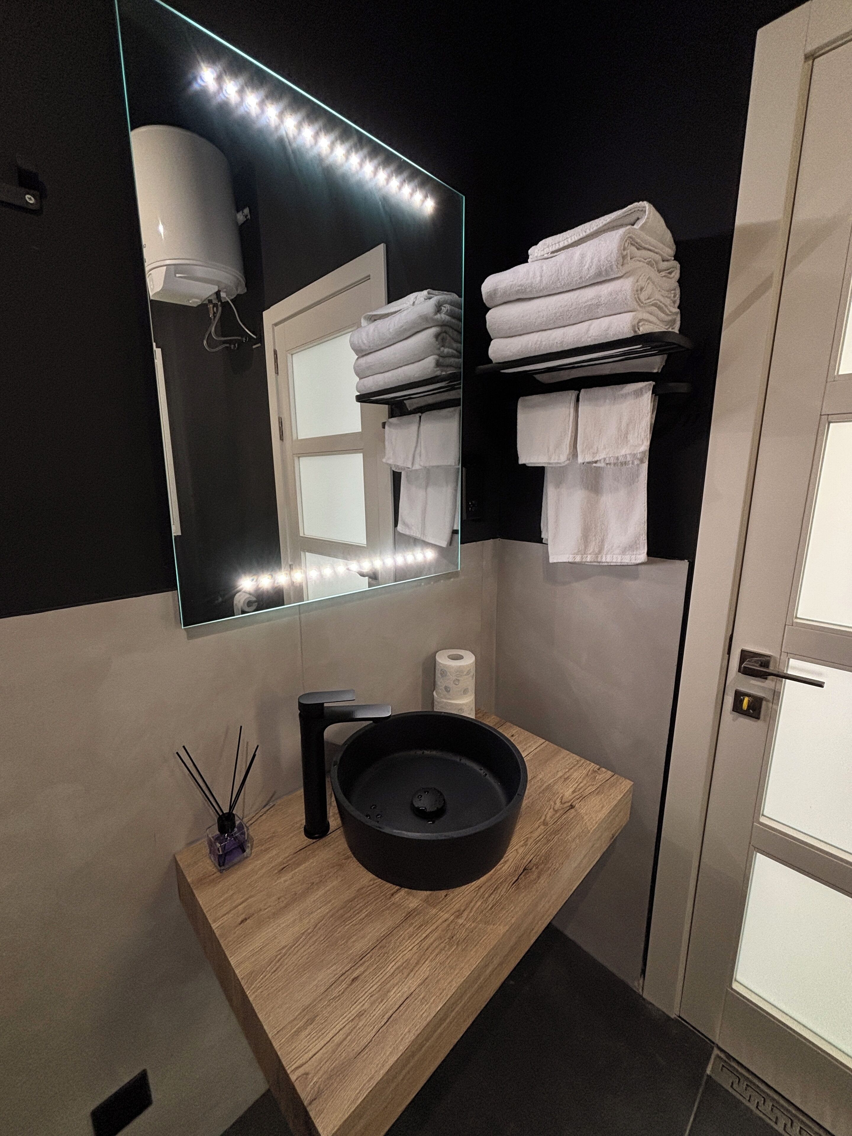 A modern bathroom with a wooden vanity, a round sink, a mirror with LED lights, and a towel rack.