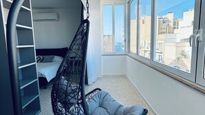 A modern room with a hanging chair, a bed, a built-in shelf, and large windows offering a city view. - 3-bed apartment in Sliema with sea views (Sliema)