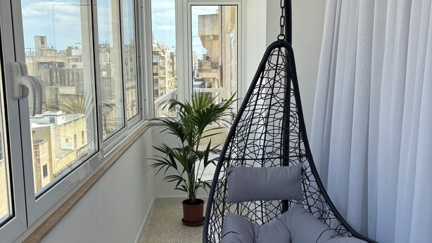 A balcony with a hanging chair, a potted plant, and a view of the cityscape. - 3-bed apartment in Sliema with sea views (Sliema)