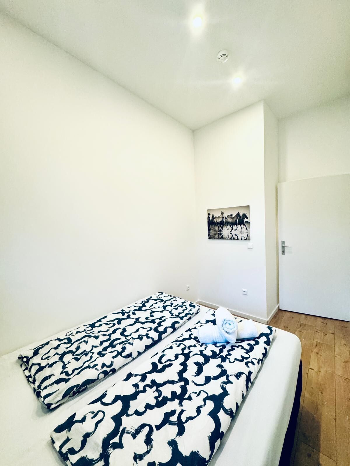 A minimalist bedroom with a bed, white walls, and a wooden floor.