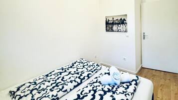 A minimalist bedroom with a bed, white walls, and a wooden floor.