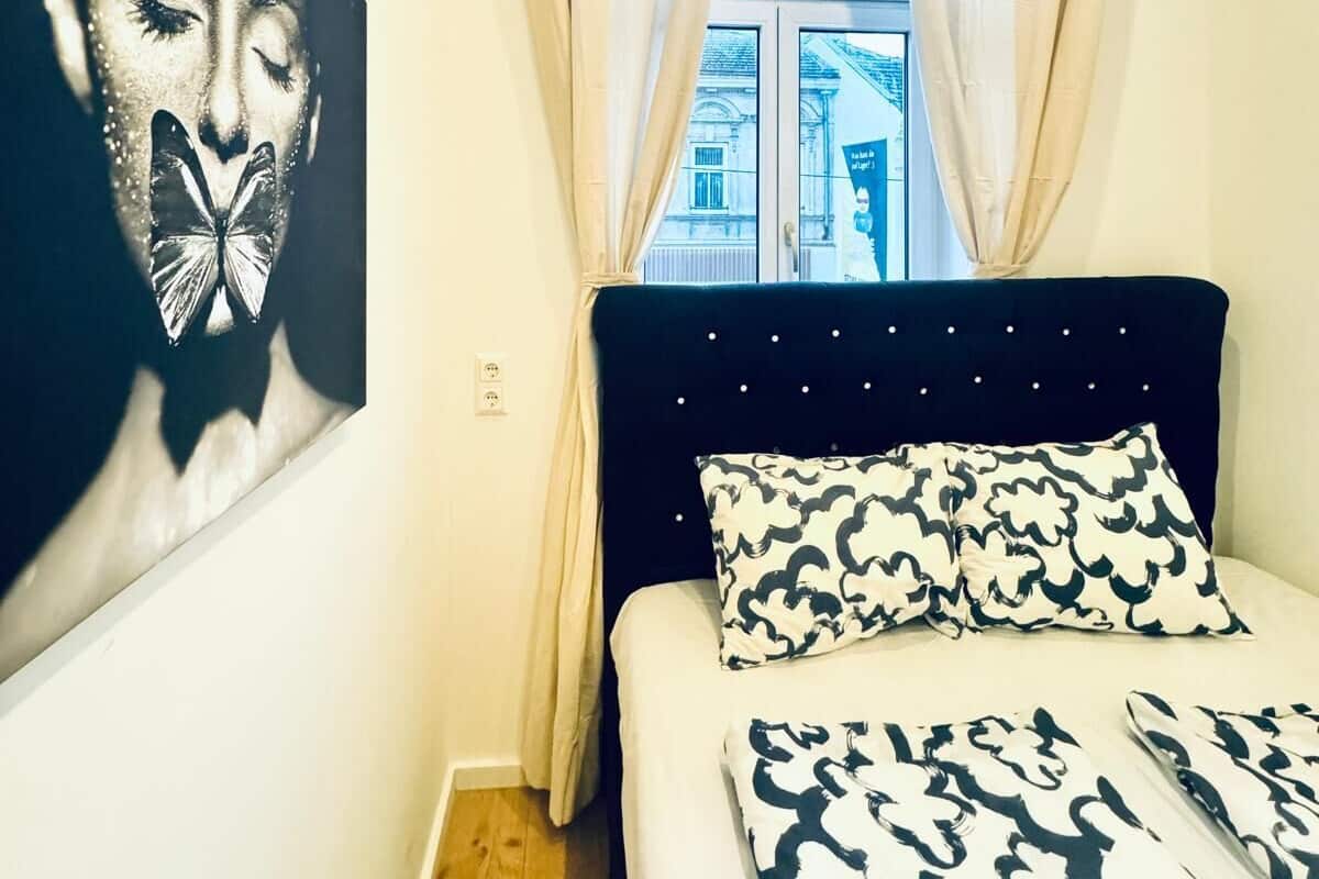 A bedroom with a bed, a window with curtains, and a wall-mounted artwork.