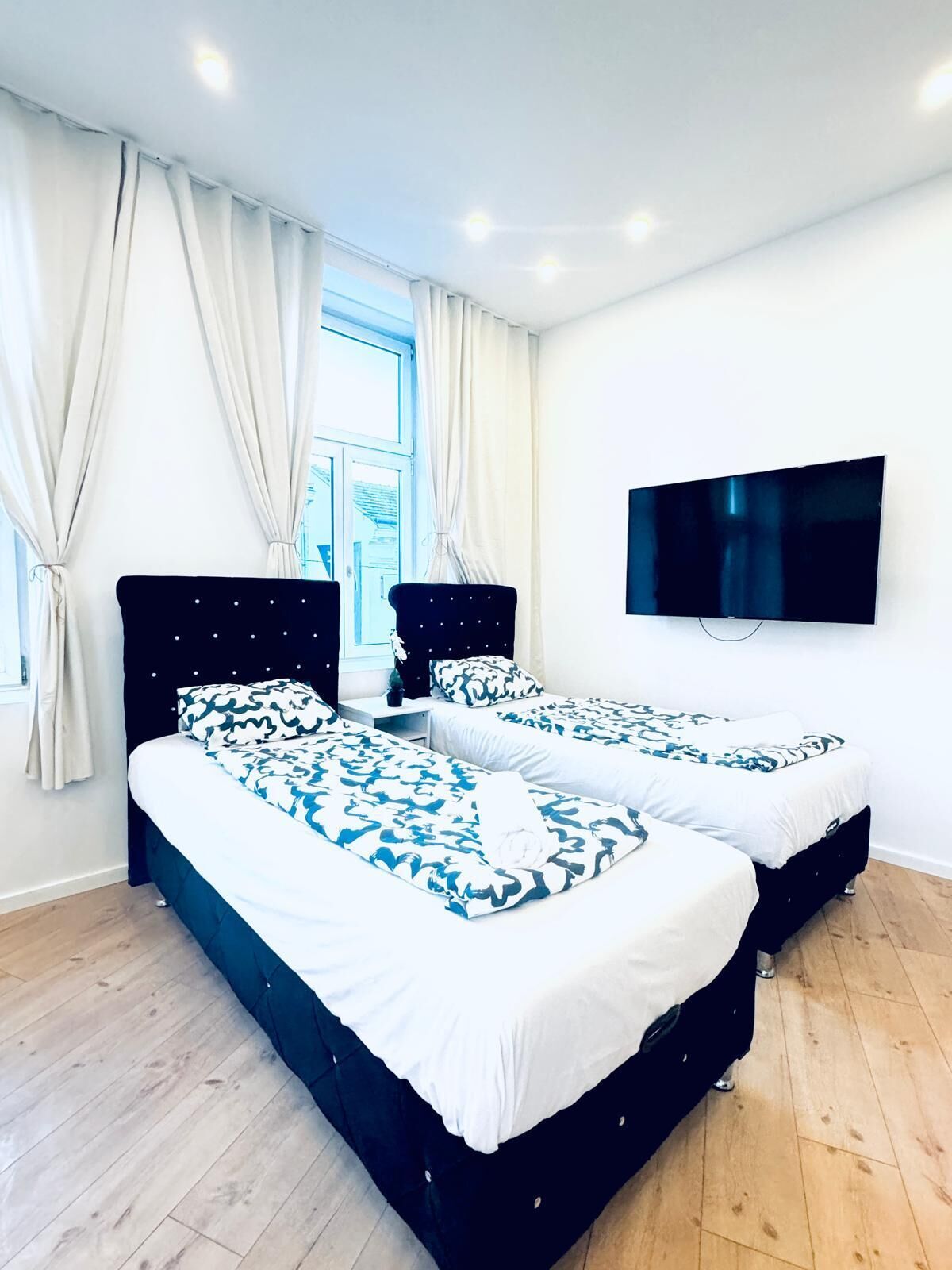 Una habitación de hotel moderna con dos camas, un televisor de pantalla plana y un gran ventanal con cortinas.
